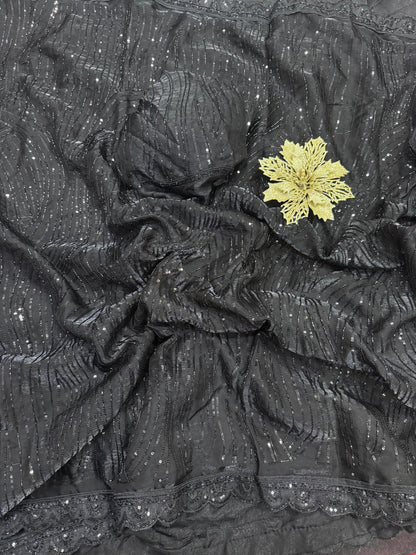 The saree in the image is crafted from sequin-embroidered net or organza fabric, layered over a smooth satin or silk-blend inner petticoat and blouse.